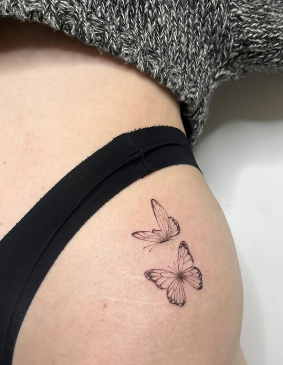 Tendencia fineline: Tatuaje estilo fineline de dos mariposas delicadas en tinta negra, dise&ntilde;o minimalista y elegante